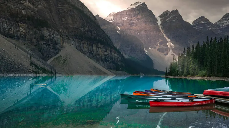 Multicolored canoes moored in dock in lake by Chi Liu